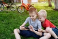 Two boys are gaming on the smartphone while sitting on the grass. Bicycles in the background Royalty Free Stock Photo