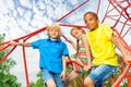 Two boys and girl sit on red ropes of playground Royalty Free Stock Photo