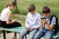 Two boys and girl use their phones during school breack. Cute boys sitting on the bench and play online games Royalty Free Stock Photo