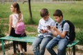 Two boys and girl use their phones during school breack. Cute boys sitting on the bench and play online games