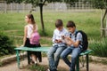 Two boys and girl use their phones during school breack. Cute boys sitting on the bench and play online games Royalty Free Stock Photo