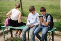 Two boys and girl use their phones during school breack. Cute boys sitting on the bench and play online games Royalty Free Stock Photo