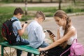 Two boys and girl use their phones during school breack. Cute boys sitting on the bench and play online games Royalty Free Stock Photo