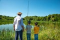 Two boys and grandfathers went fishing. They stand on the shore of the pond and look into the distance