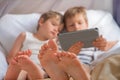 Two boys holding smartphone, tablet sitting on chair, focus on childrens feet.