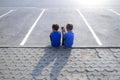 Two boys with mobile phone sitting in an empty parking. Childhood, education, learning, technology, leisure concept