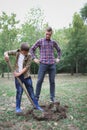 Two brothers a dig earth in a park for planting young tree. Family work, autumn day. Royalty Free Stock Photo