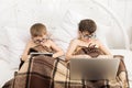 Two boys play at laptop and tablet with dog in bed Royalty Free Stock Photo