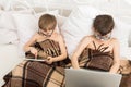 Two boys play at laptop and tablet with dog in bed Royalty Free Stock Photo