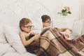 Two boys play at laptop and tablet with dog in bed Royalty Free Stock Photo