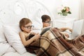 Two boys play at laptop and tablet with dog in bed Royalty Free Stock Photo