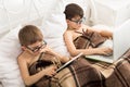 Two boys play at laptop and tablet with dog in bed Royalty Free Stock Photo