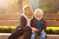 Two boys playing internet games with mobile smartphone outdoors. Brothers sit on a bench and usinf mobile phone Royalty Free Stock Photo