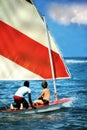 Two boys sailing on small sailboat in blue ocean