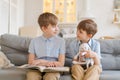 Two boys sitting on couch are reading book. Older brother reads interesting Royalty Free Stock Photo
