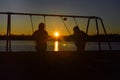 Two Boys on Swings with Sunset over Lake Royalty Free Stock Photo