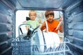 Two boys together take dishes form the dishwasher