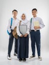 two boys and a veiled girl in junior high school uniforms stand smiling carrying a laptop computer, backpack, and a book