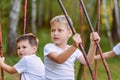 Two boys in white t-shirts ride a swing in the summer