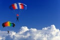 Two Parachutists Soar On Colorful Parachutes Across The Boundless Blue Sky Against The Background Of White Fluffy Clouds