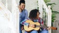 Two brazilian curly girls sistres sitting on stairs and practice to play acoustic guitar. Friends have fun and singing Royalty Free Stock Photo