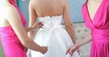 Two bride-maids in fuchsia dresses bustling the wedding dress. Bride-maids hands ribbon making on the back of bride white dress