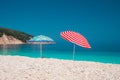 Two bright colored sun beach umbrella on pebble beach against turquoise blue sea water surface and clean blue sky Royalty Free Stock Photo