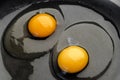 Two bright round yolks in raw whites, uncooked small fried eggs is a simple breakfast in a black skillet. Top view