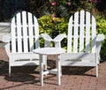 Two white Adirondack chairs on a brick outdoorpation