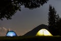 Two brightly lit tourist tents on green grassy forest clearing on dark mountain and clear blue starry sky copy space background. Royalty Free Stock Photo