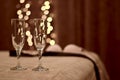 Two shiny wine glasses closer on the bed and blurry silhouettes of clothes in the bedroom with bokeh fires.