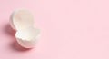 Two broken white eggshell halves are placed on a pastel pink background. The Royalty Free Stock Photo