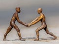 Two bronze figurines standing on sandy ground, holding hands in a gesture of connection and solidarity Royalty Free Stock Photo
