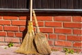 Two brooms on the background of a brick foundation of a rural house in the rays of the bright sun