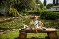 Two brother boys sitting on a bench in a park near peaceful lake with water lily Nymphaeum. Kids relaxing on nature on hot summer Royalty Free Stock Photo