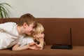 Two brothers lying on couch and stare at laptop monitor. Children watch cartoons