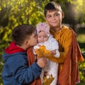 Two brothers - older and younger, hold their sister - baby in their arms, kissing her, autumn walk