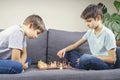 Two brothers are playing chess game while sitting on the couch. Strategic board game, leisure, entertainment at home Royalty Free Stock Photo