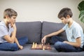 Two brothers are playing chess game while sitting on the couch. Strategic board game, leisure, entertainment at home Royalty Free Stock Photo