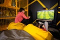 Two brothers playing football video game console, sitting on yellow pouf in kids play center Royalty Free Stock Photo