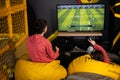 Two brothers playing football video game console, sitting on yellow pouf in kids play center Royalty Free Stock Photo