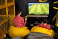 Two brothers playing football video game console, sitting on yellow pouf in kids play center Royalty Free Stock Photo