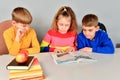 Two brothers and sister are reading a book on a white table Royalty Free Stock Photo