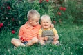 Two brothers sitting together on grass in park outside sharing apple. Older brother hug calm down soothe pacify crying younger