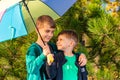 Two brothers stand in an embrace under a bright multi-colored umbrella and look at each other in a pine forest