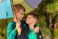 Two brothers stand in an embrace under a bright multi-colored umbrella and look at each other in a pine forest