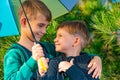 Two brothers stand in an embrace under a bright multi-colored umbrella and look at each other in a pine forest