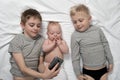 Two brothers with a youngest child are lying on a white bed and taking selfie on a smartphone. Happy childhood, big family Royalty Free Stock Photo