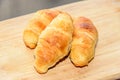 Two brown baked croissants, wooden plate, close up