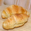 Two brown baked croissants, wooden plate, close up